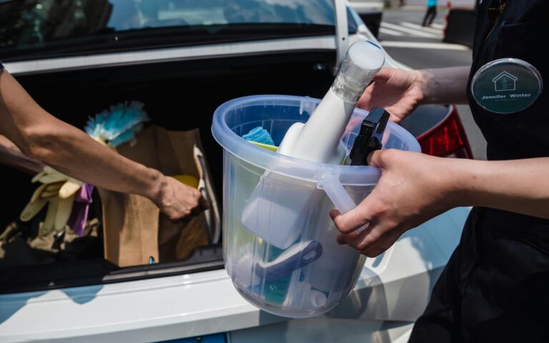 Close-up of cleaning supplies in a bucket near a car trunk, outdoors.